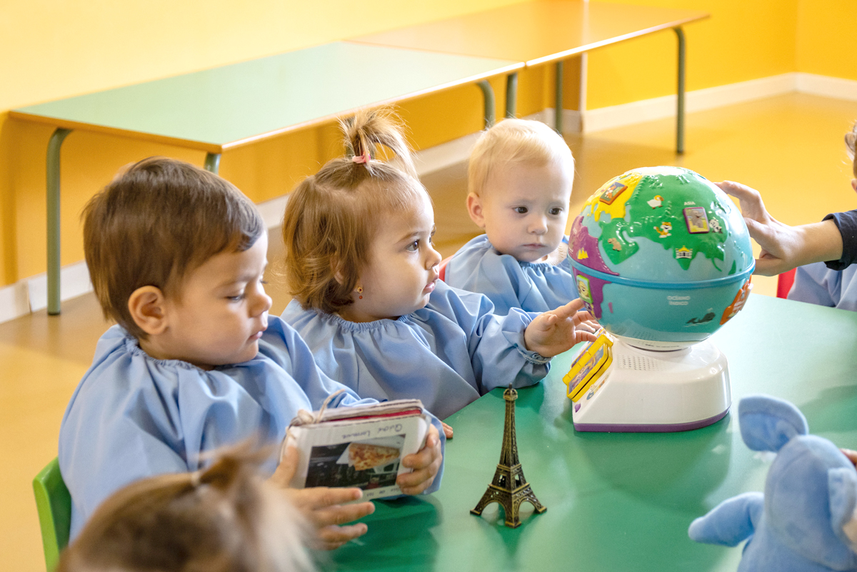 Niños pequeños en una escuela infantil observando con admiración e intriga un juguete con la forma de la bola del mundo.