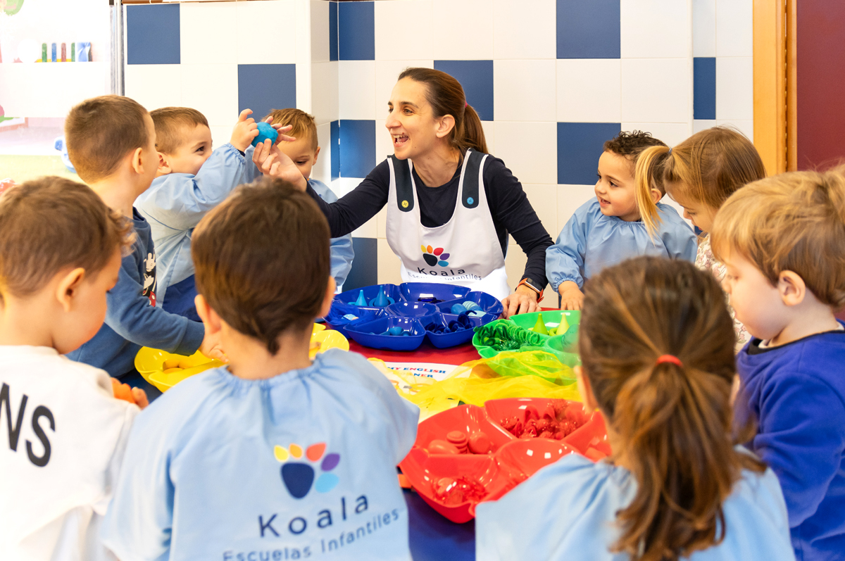 Educadora infantil de koala mostrando piezas de diferentes colores y formas a los niños de su escuela.